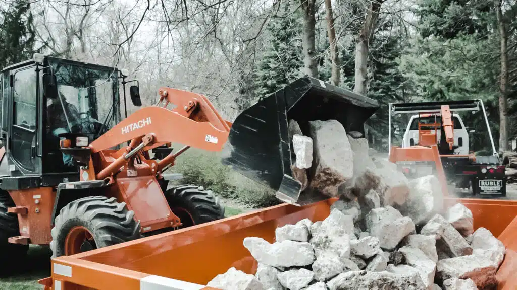A Kubota backhoe loading rocks into a dump truck for Salt Dumpster rental in Salt Lake City.
